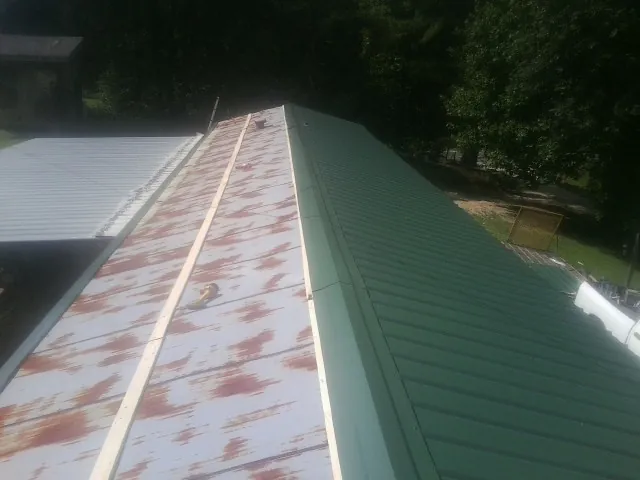 Old rusted panels beside newly installed green metal roofing — Wind Damage Roof Repair by Roofing Brothers in Gray