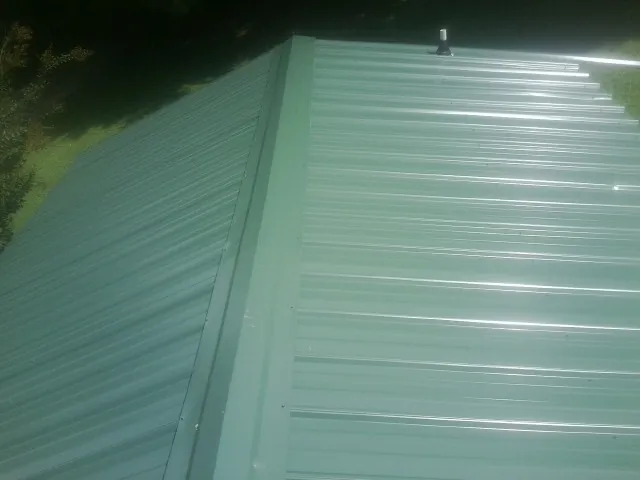 New green metal panels meeting at the ridge of a roof — Flat Roof Repair work by our crew in Gray